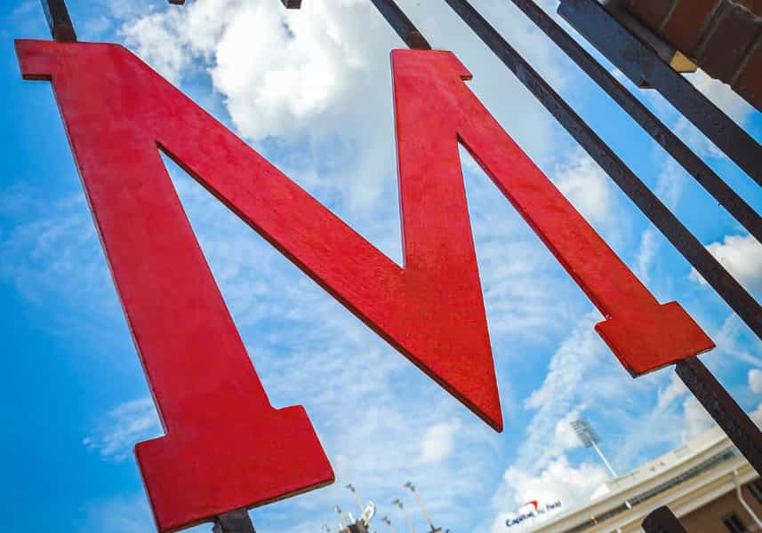 Congress Passes FY25 Continuing Resolution to Fund Federal Programs Through the End of the Fiscal Year: Wrought iron red M Gate against brick outside of Maryland Stadium.